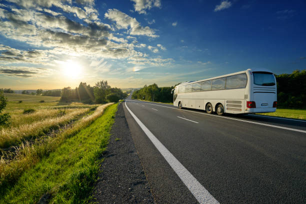 White bus traveling on the asphalt road in a rural landscape at sunset